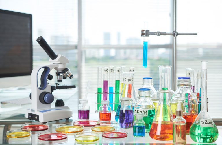 Modern Laboratory Interior Interior of modern laboratory: desk with Petri dishes, test tubes, flasks and modern microscope on foreground, panoramic windows with blinds on background